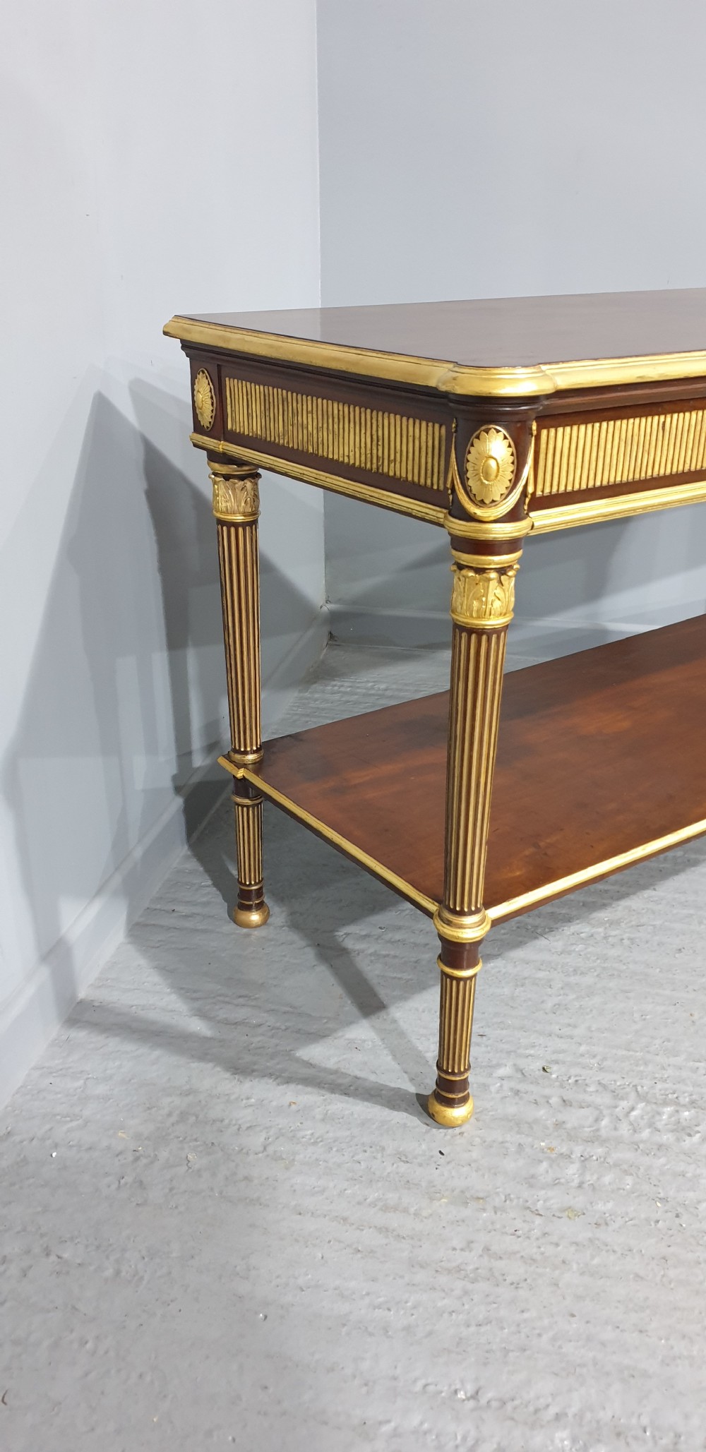 A dark mahogany rectangular console table featuring giltwood fluted legs, a lower shelf, and gold carved swags along the front apron. View VI