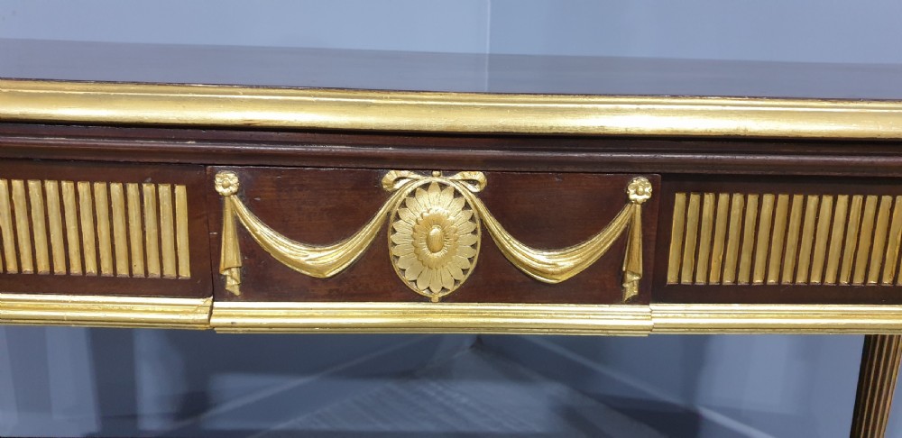 A dark mahogany rectangular console table featuring giltwood fluted legs, a lower shelf, and gold carved swags along the front apron. View VII