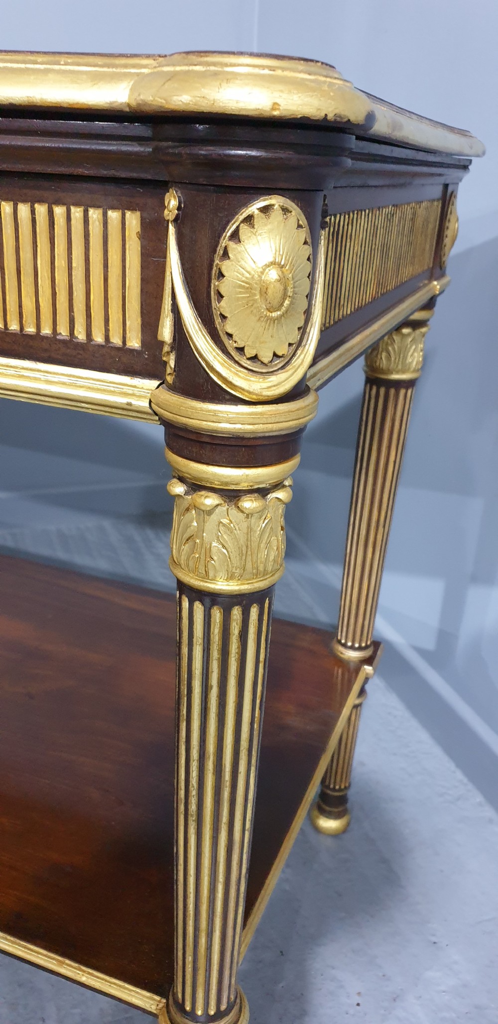 A dark mahogany rectangular console table featuring giltwood fluted legs, a lower shelf, and gold carved swags along the front apron. View VIII