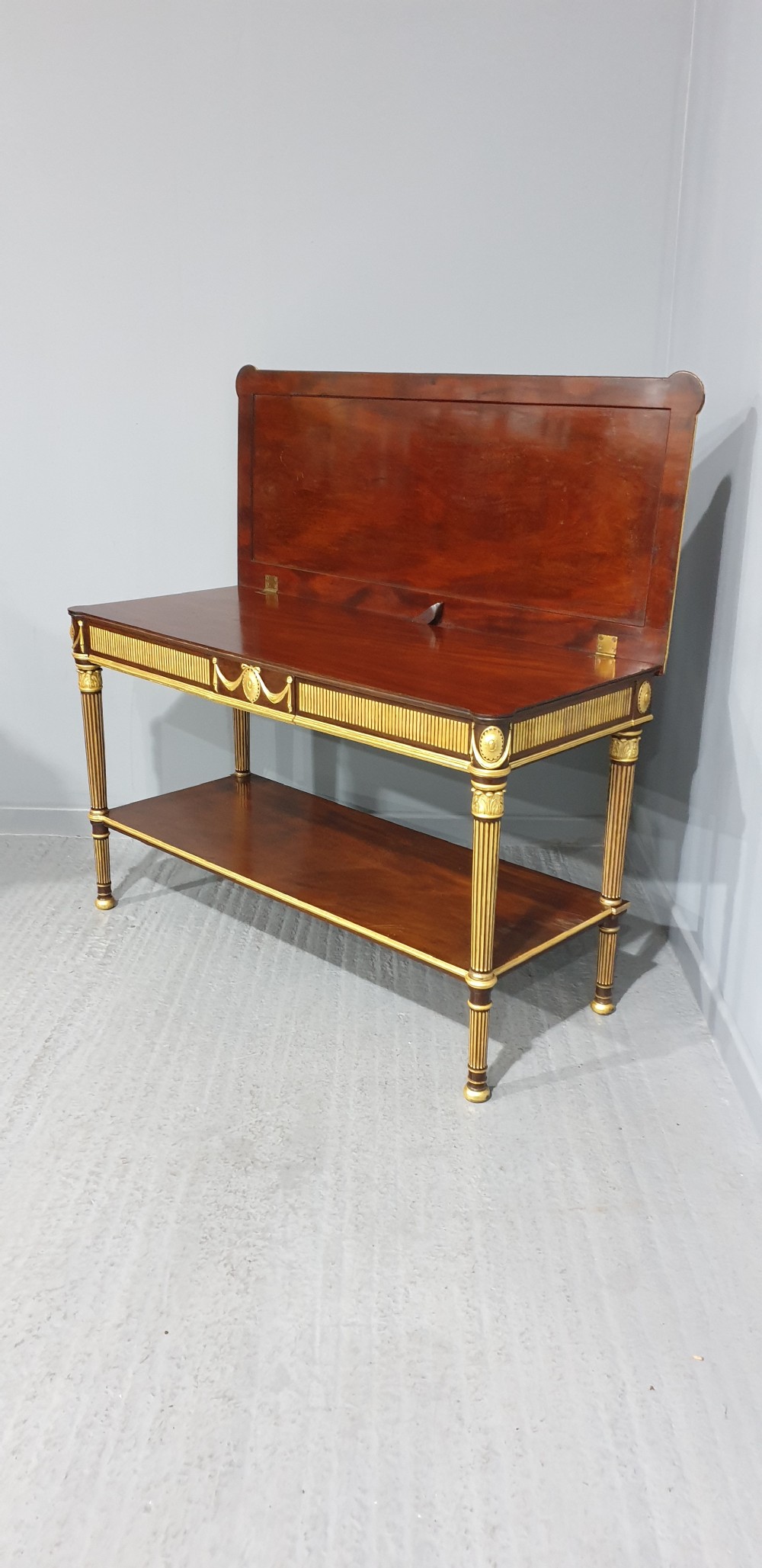 A dark mahogany rectangular console table featuring giltwood fluted legs, a lower shelf, and gold carved swags along the front apron. View XI