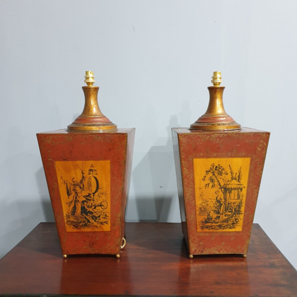 A pair of tapered rectangular red and gold lacquered toleware table lamps decorated with hand-painted chinoiserie figures and brass fittings.
