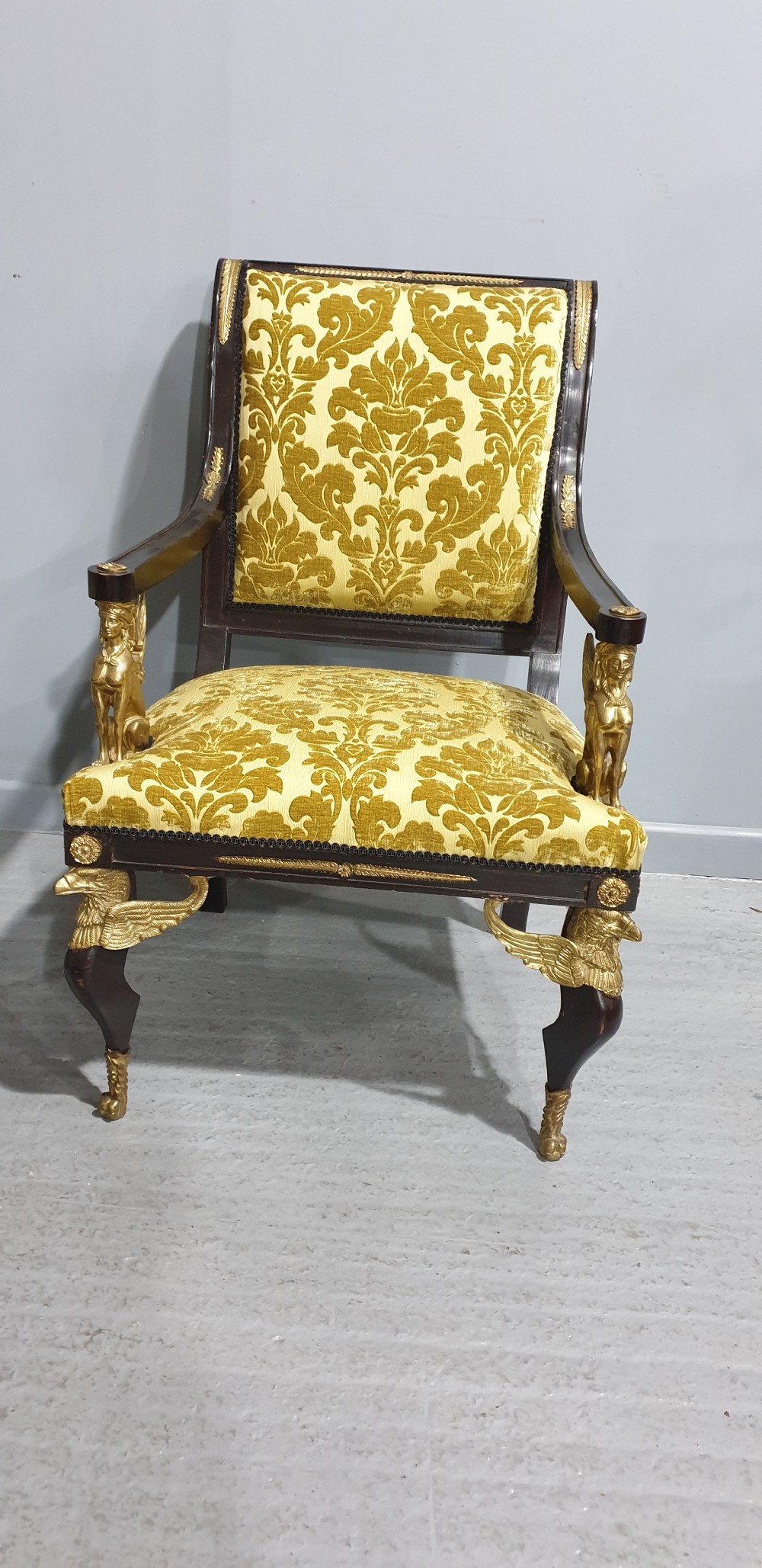 A pair of French Empire armchairs crafted with dark ebonised frames, gilded ormolu caryatid mounts, and patterned gold damask upholstery. View II