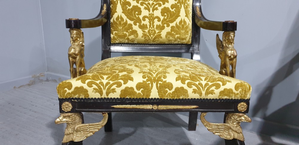 A pair of French Empire armchairs crafted with dark ebonised frames, gilded ormolu caryatid mounts, and patterned gold damask upholstery. View V