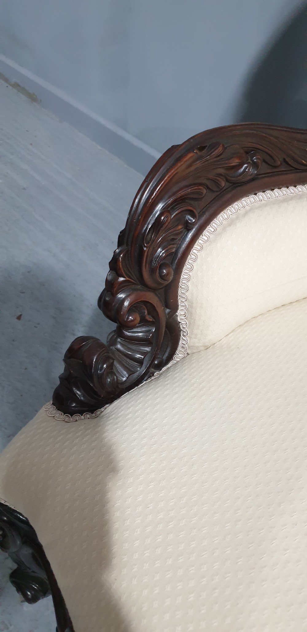 An antique Victorian dark mahogany armchair featuring an ornate floral carved crest, button-tufted cream upholstery, and carved cabriole legs on castors. View V
