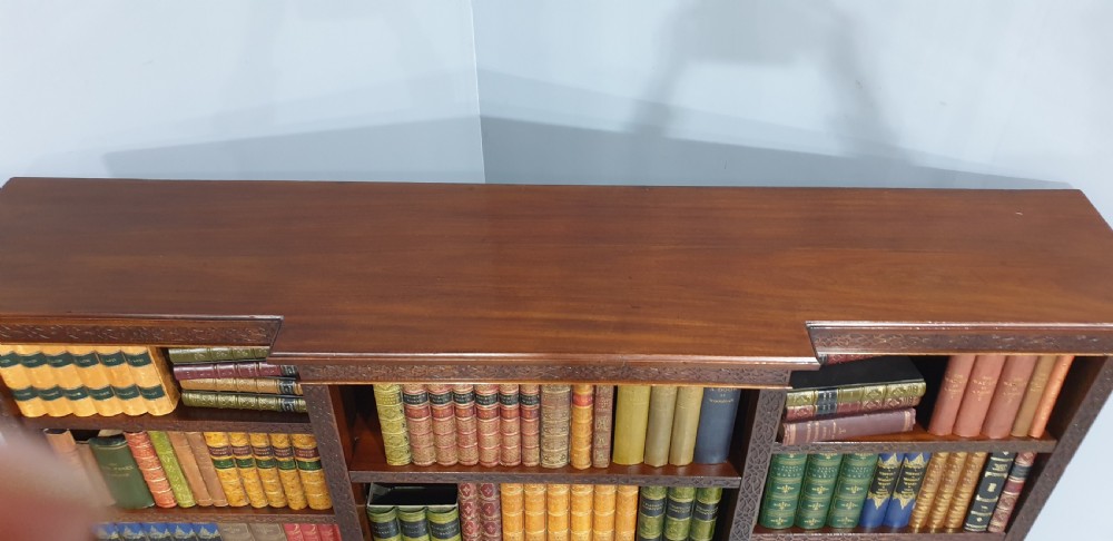 A low, wide mahogany breakfront open bookcase featuring three sections of adjustable shelves with carved fretwork detail along the top edge. View X