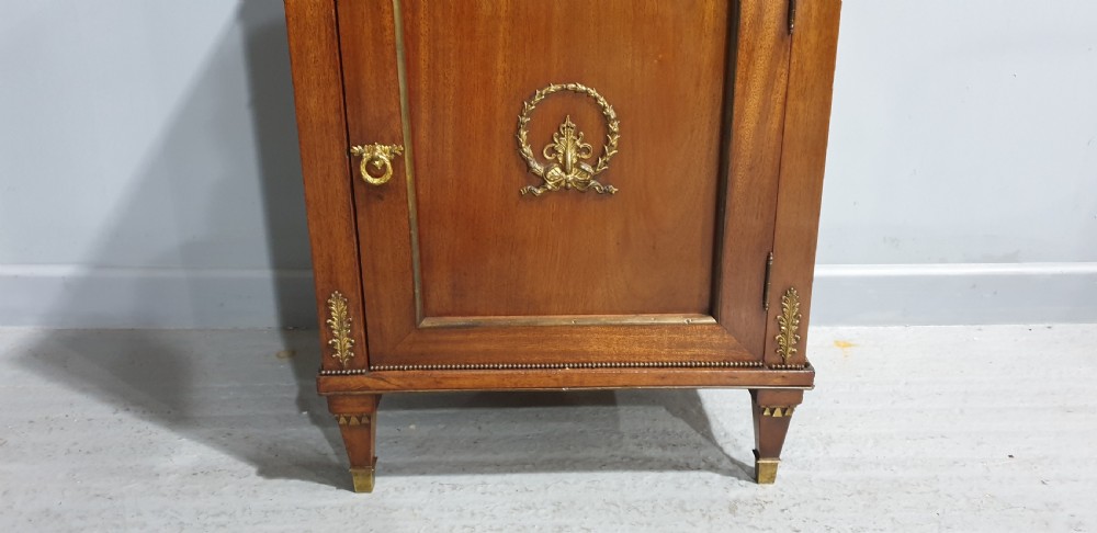 An antique French Empire style mahogany side cabinet featuring a single top drawer, a lower cupboard door decorated with a brass laurel wreath mount, and square tapered legs with brass feet. View III