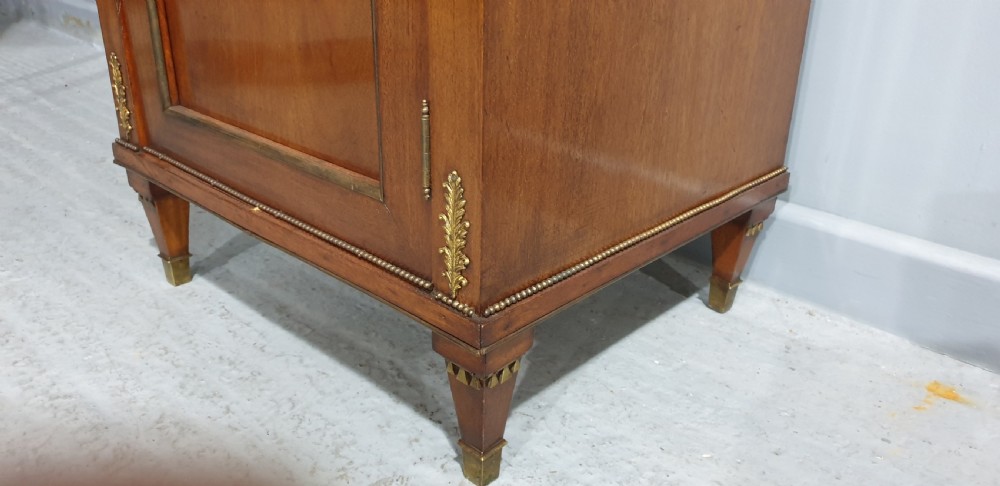 An antique French Empire style mahogany side cabinet featuring a single top drawer, a lower cupboard door decorated with a brass laurel wreath mount, and square tapered legs with brass feet. View VIII