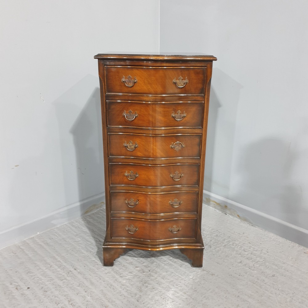 A tall, narrow mahogany chest of drawers featuring a serpentine front with six drawers and decorative brass drop handles.