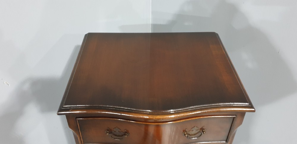 A tall, narrow mahogany chest of drawers featuring a serpentine front with six drawers and decorative brass drop handles. View V
