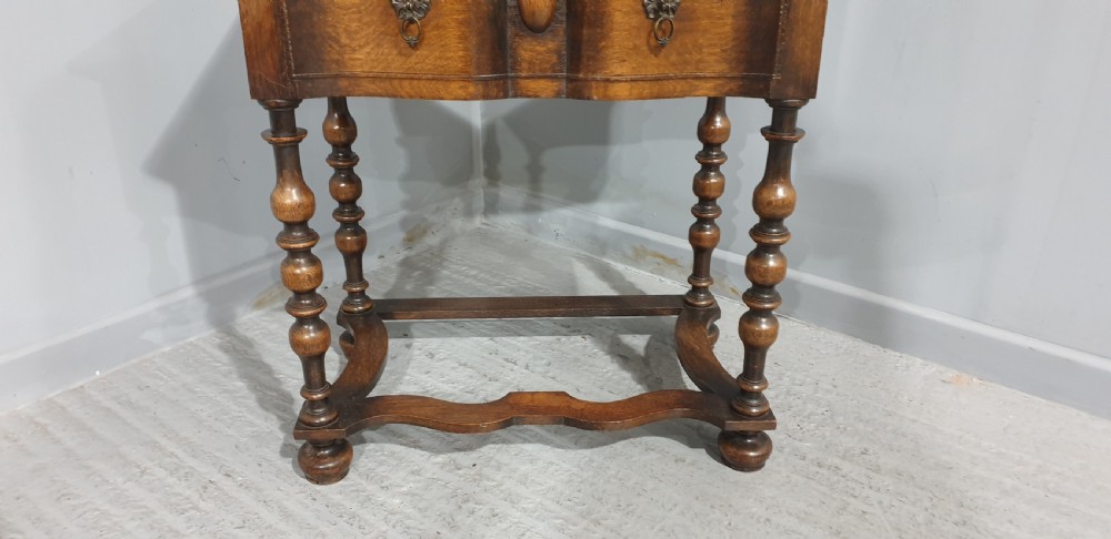 An antique oak side table featuring bobbin turned legs, a shaped frieze drawer with brass drop handles, and a wavy cross-stretcher base. View III