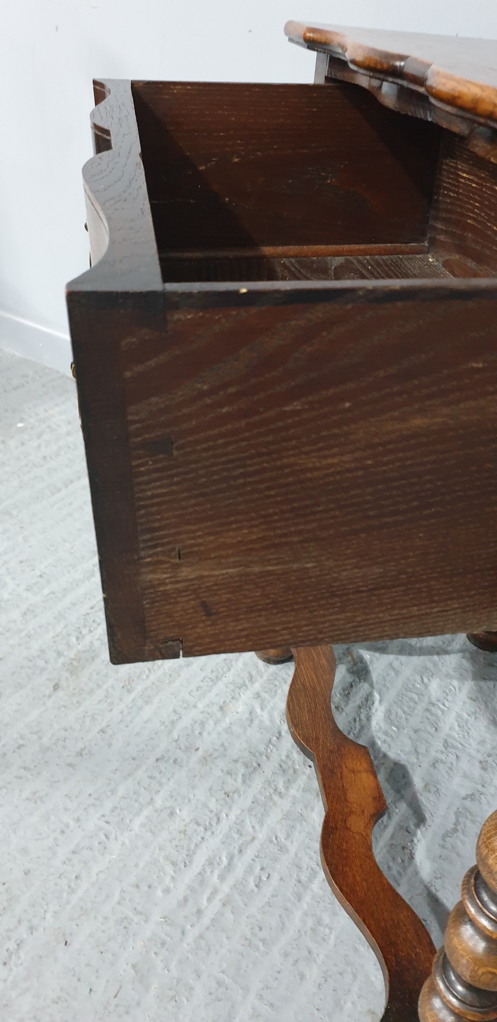 An antique oak side table featuring bobbin turned legs, a shaped frieze drawer with brass drop handles, and a wavy cross-stretcher base. View IX