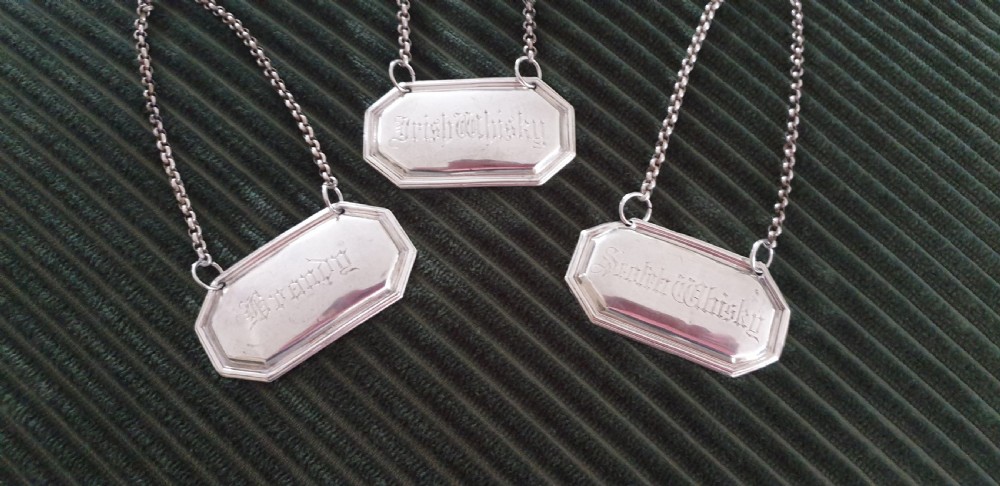 A set of three octagonal silver decanter labels with fine link chains, engraved with Brandy, Irish Whisky, and Scotch Whisky in Gothic script. View III
