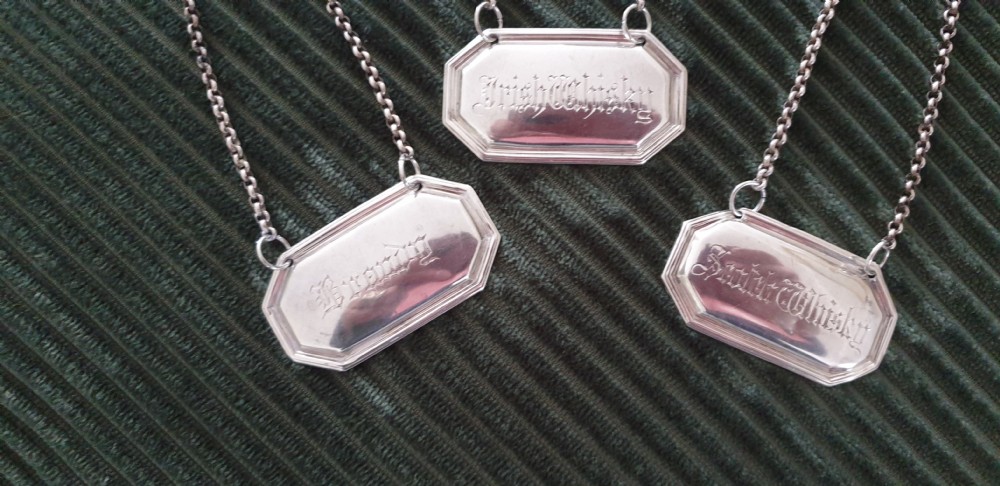 A set of three octagonal silver decanter labels with fine link chains, engraved with Brandy, Irish Whisky, and Scotch Whisky in Gothic script. View II