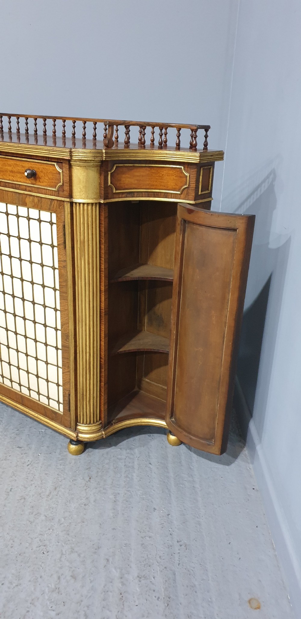 A Regency rosewood side cabinet featuring a spindle gallery rail, gilt brass trim, upper drawers, and fabric panel doors with brass lattice. View III