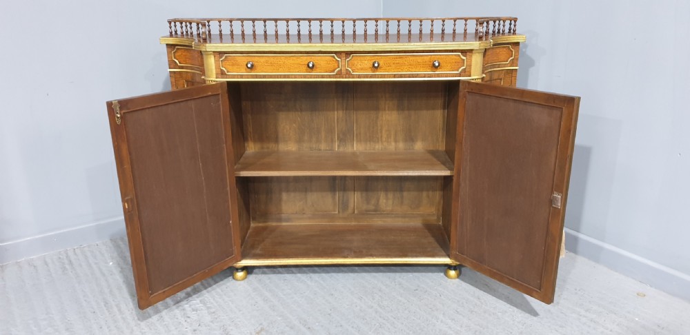 A Regency rosewood side cabinet featuring a spindle gallery rail, gilt brass trim, upper drawers, and fabric panel doors with brass lattice. View VI