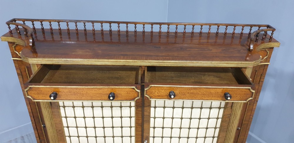 A Regency rosewood side cabinet featuring a spindle gallery rail, gilt brass trim, upper drawers, and fabric panel doors with brass lattice. View VIII