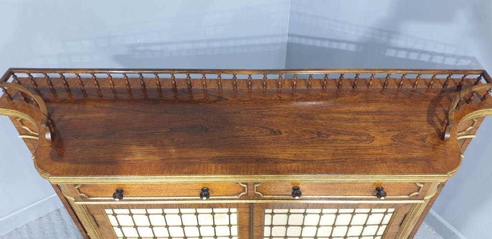 A Regency rosewood side cabinet featuring a spindle gallery rail, gilt brass trim, upper drawers, and fabric panel doors with brass lattice. View X