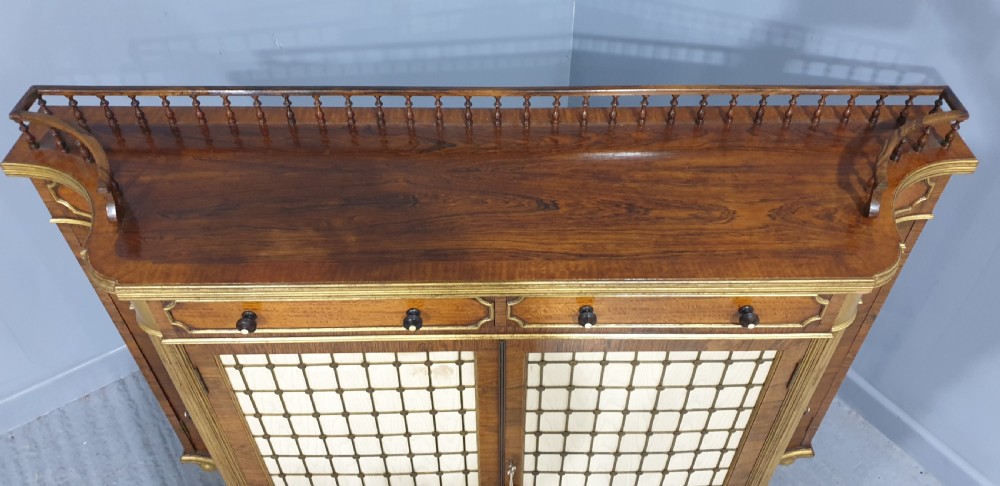 A Regency rosewood side cabinet featuring a spindle gallery rail, gilt brass trim, upper drawers, and fabric panel doors with brass lattice. View XI