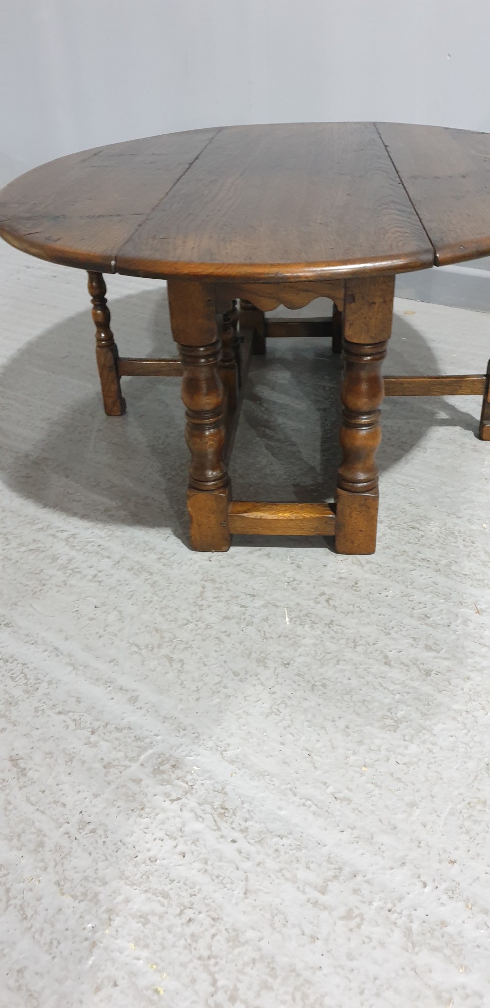 A low solid oak oval coffee table featuring turned gateleg supports and a warm brown timber patina. View VII