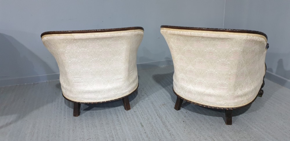 A pair of Victorian mahogany hoop-backed easy chairs upholstered in cream patterned damask fabric with carved legs on brass castors. View X