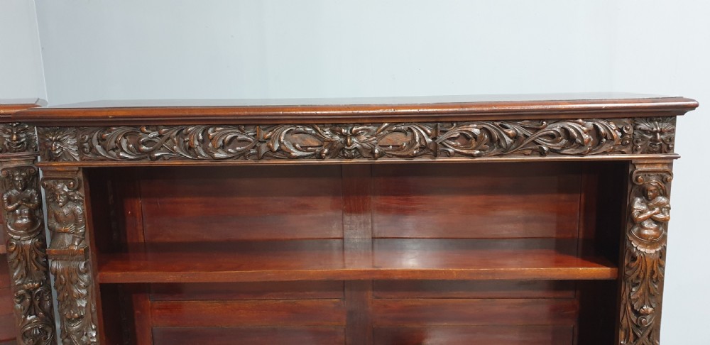 A pair of low mahogany open library bookcases featuring carved friezes, pilasters, and three adjustable shelves on plinth bases. View VII
