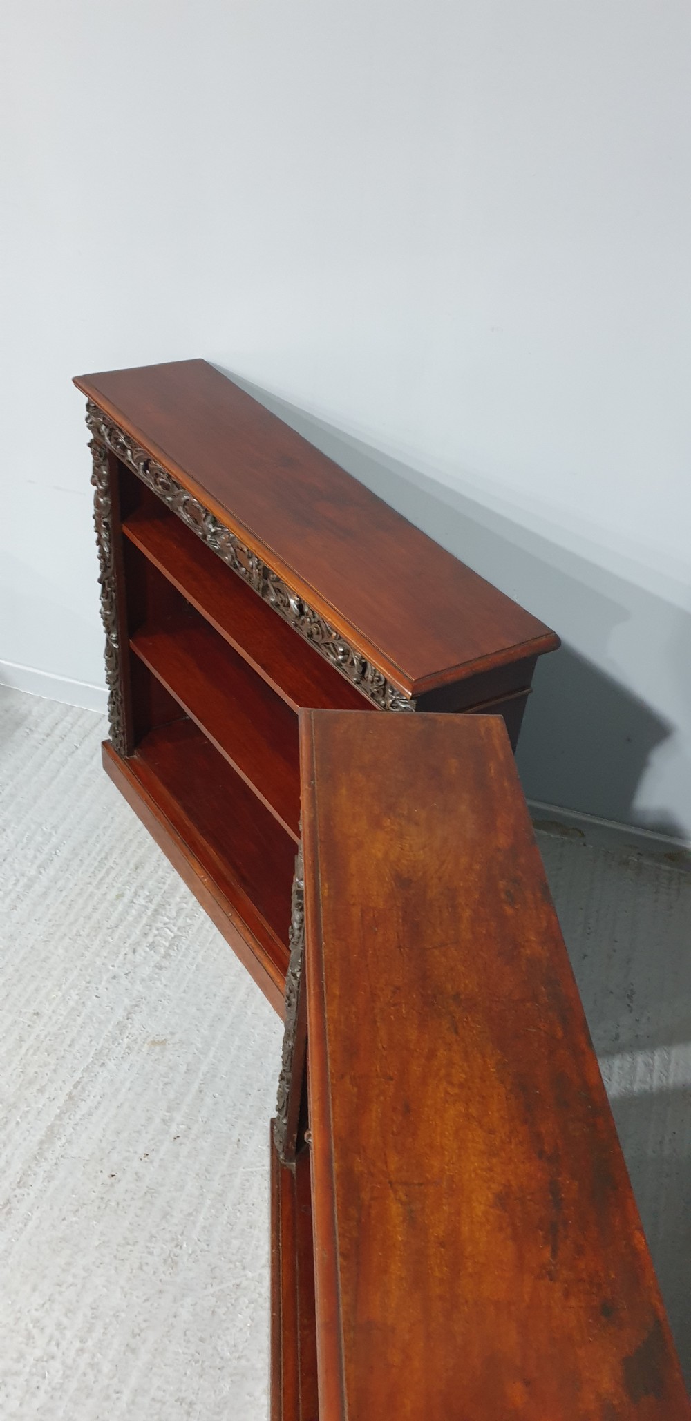 A pair of low mahogany open library bookcases featuring carved friezes, pilasters, and three adjustable shelves on plinth bases. View X