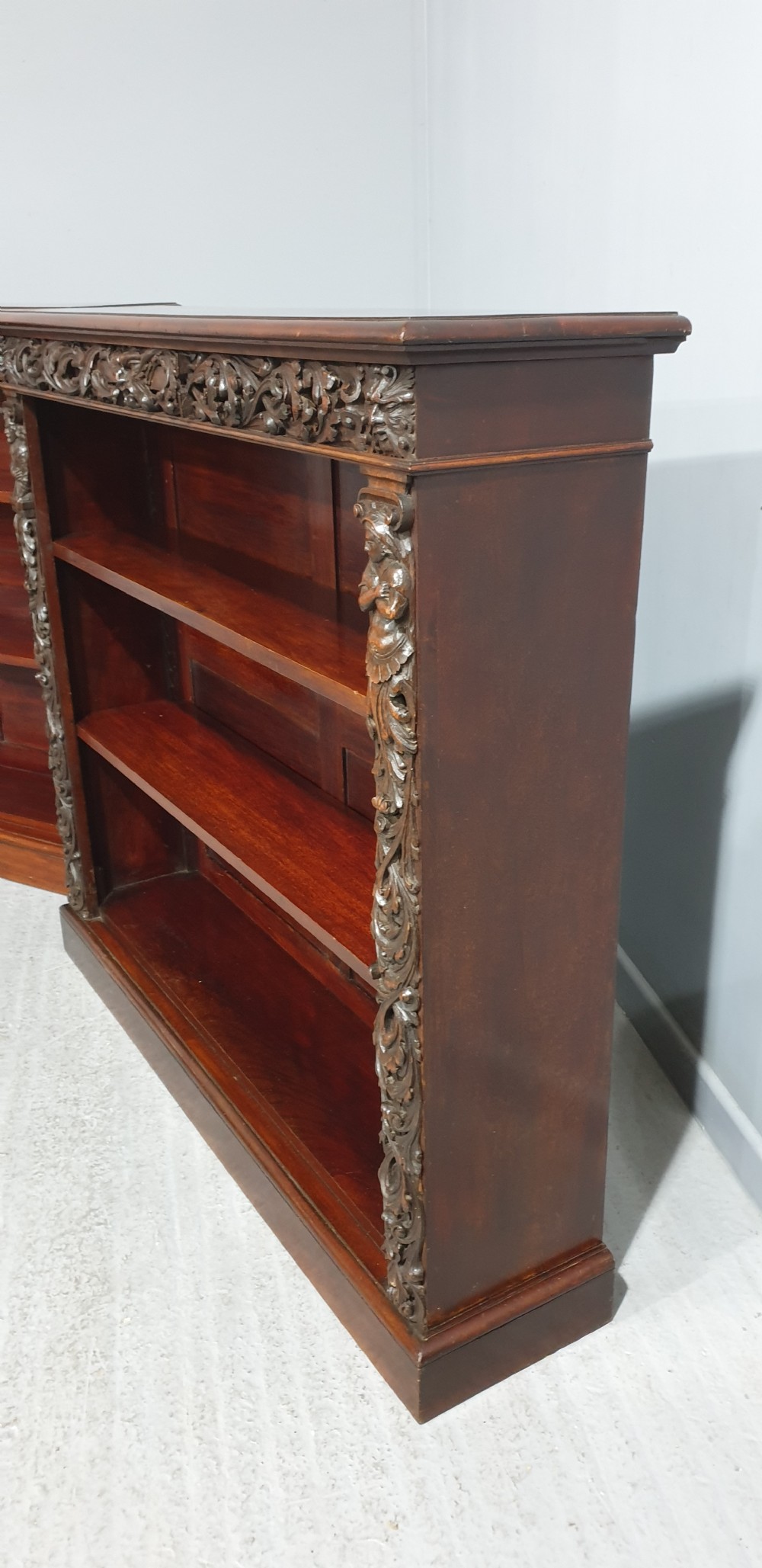 A pair of low mahogany open library bookcases featuring carved friezes, pilasters, and three adjustable shelves on plinth bases. View XI