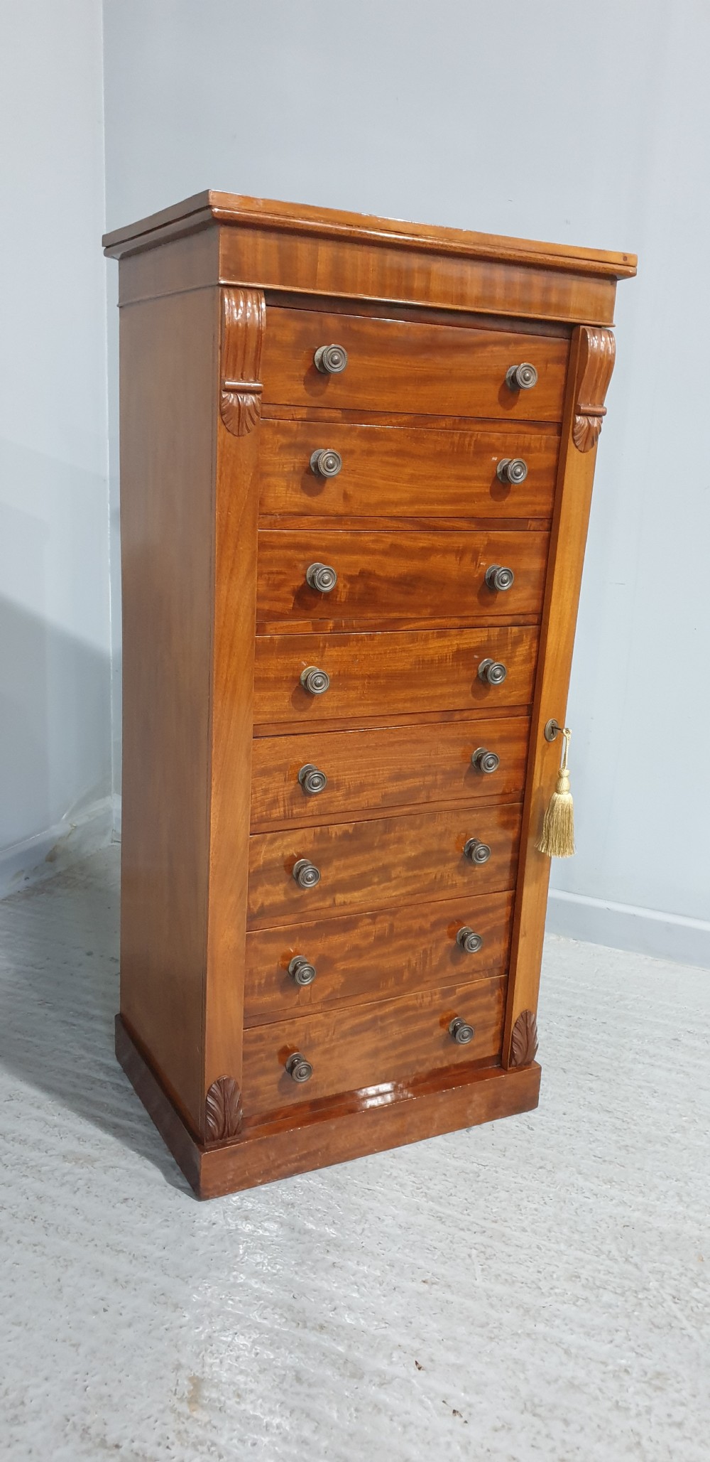 A tall Victorian flame mahogany Wellington chest of drawers featuring eight stacked drawers with turned knobs, flanked by side stiles with carved corbels. View II