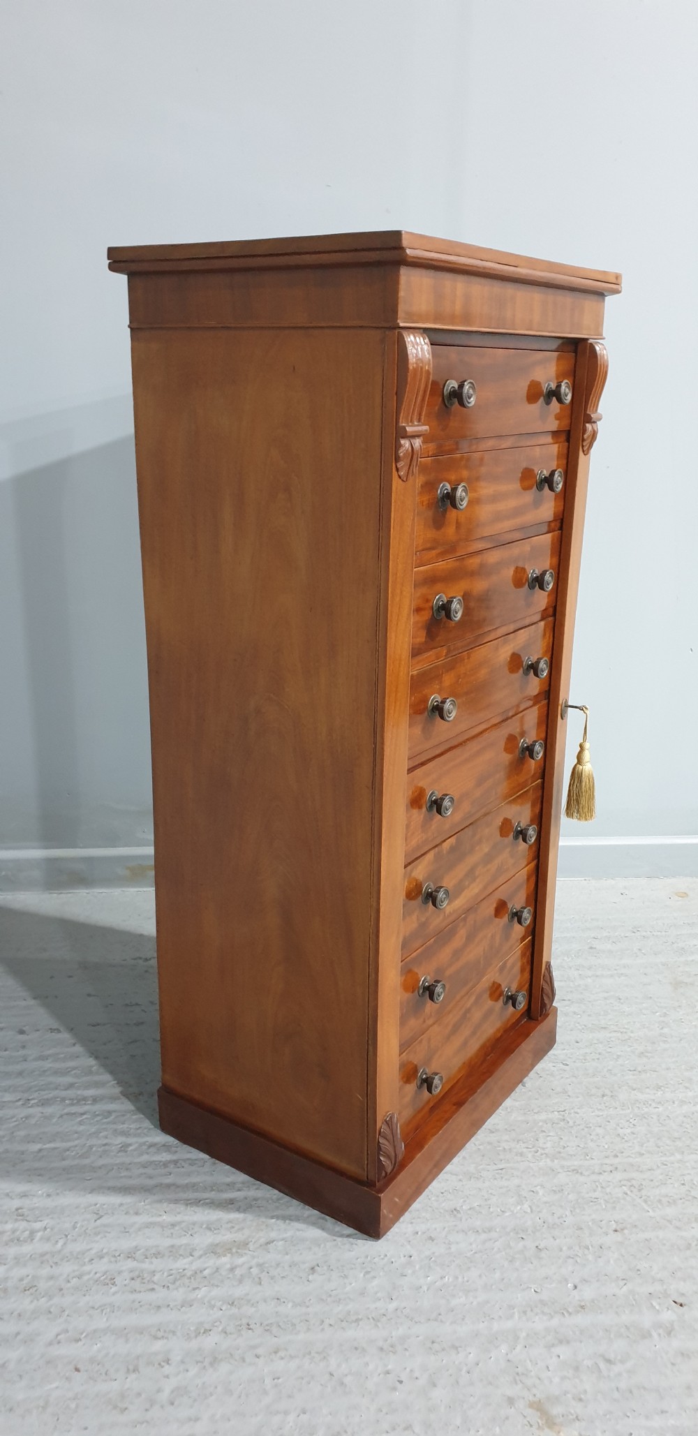 A tall Victorian flame mahogany Wellington chest of drawers featuring eight stacked drawers with turned knobs, flanked by side stiles with carved corbels. View III