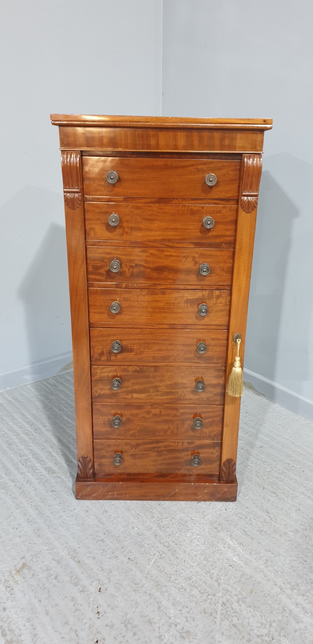 A tall Victorian flame mahogany Wellington chest of drawers featuring eight stacked drawers with turned knobs, flanked by side stiles with carved corbels. View V