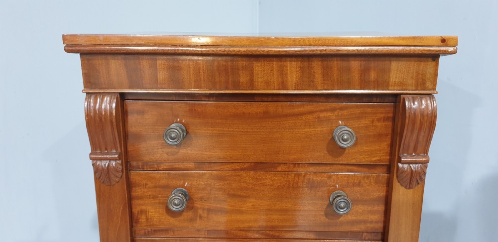 A tall Victorian flame mahogany Wellington chest of drawers featuring eight stacked drawers with turned knobs, flanked by side stiles with carved corbels. View VI