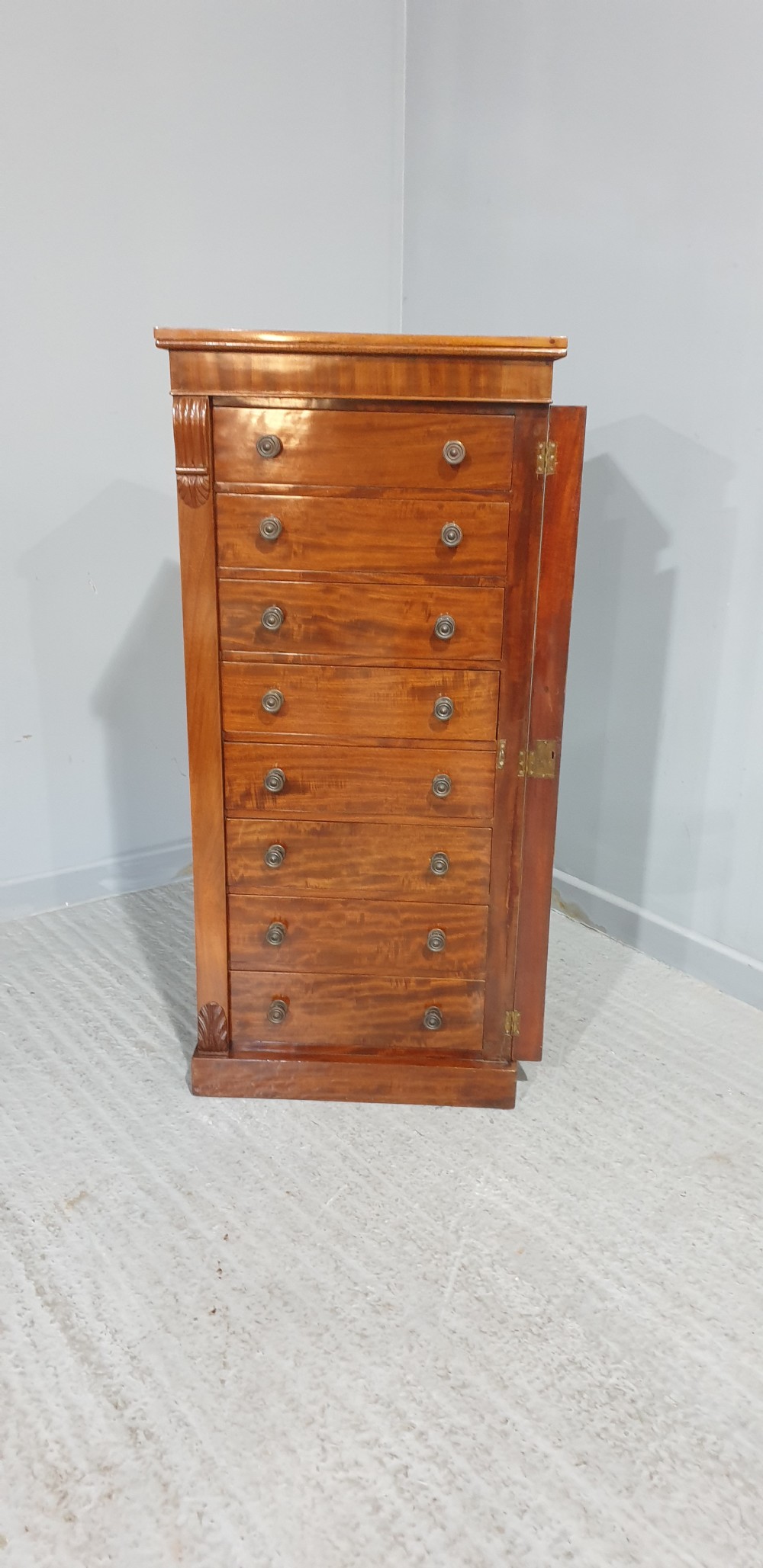 A tall Victorian flame mahogany Wellington chest of drawers featuring eight stacked drawers with turned knobs, flanked by side stiles with carved corbels. View XI