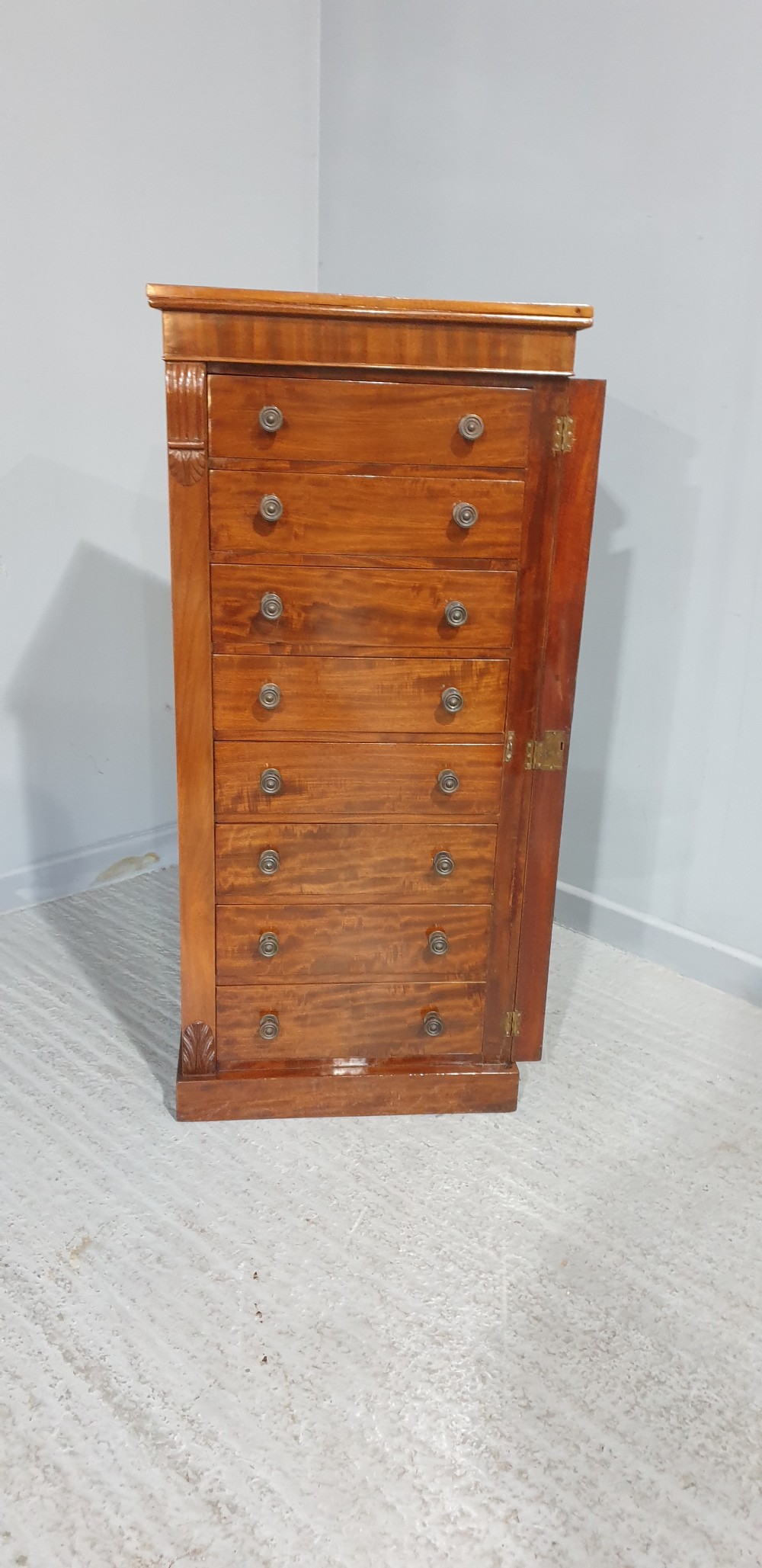 A tall Victorian flame mahogany Wellington chest of drawers featuring eight stacked drawers with turned knobs, flanked by side stiles with carved corbels. View XII