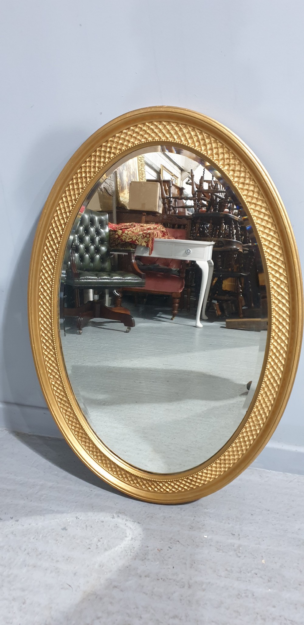 An oval Victorian wall mirror featuring a gilt gold frame with a textured lattice pattern surrounding the reflective glass mirror plate.