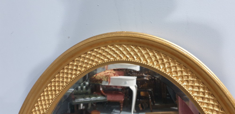 An oval Victorian wall mirror featuring a gilt gold frame with a textured lattice pattern surrounding the reflective glass mirror plate. View IV
