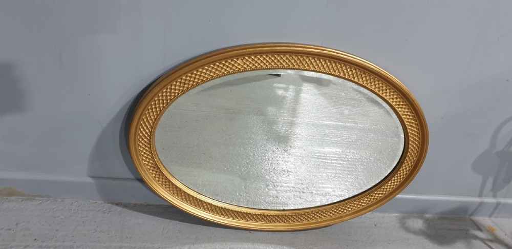 An oval Victorian wall mirror featuring a gilt gold frame with a textured lattice pattern surrounding the reflective glass mirror plate. View V