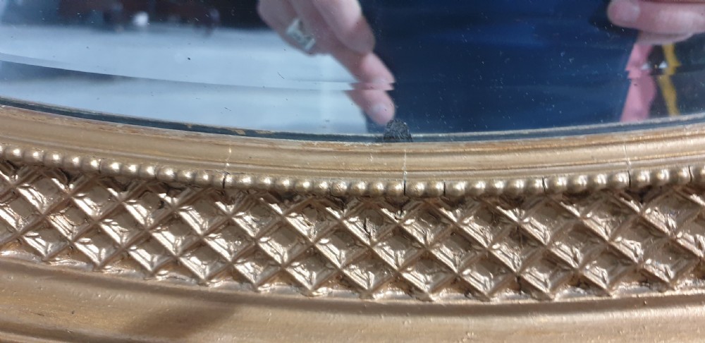 An oval Victorian wall mirror featuring a gilt gold frame with a textured lattice pattern surrounding the reflective glass mirror plate. View VII