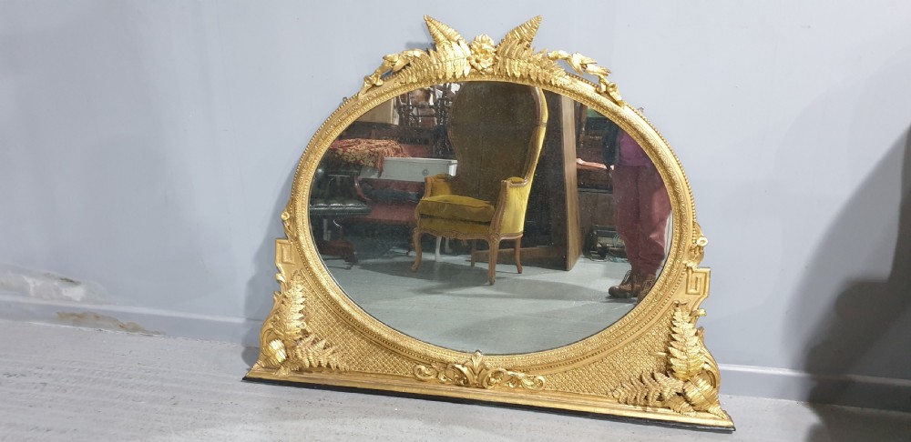 A large High Victorian arched overmantel mirror featuring a gold gilded frame decorated with carved fern leaf motifs, floral cresting, and geometric spandrel detailing. View II