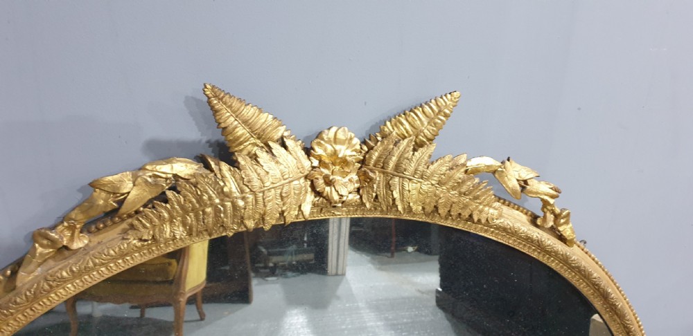 A large High Victorian arched overmantel mirror featuring a gold gilded frame decorated with carved fern leaf motifs, floral cresting, and geometric spandrel detailing. View IV