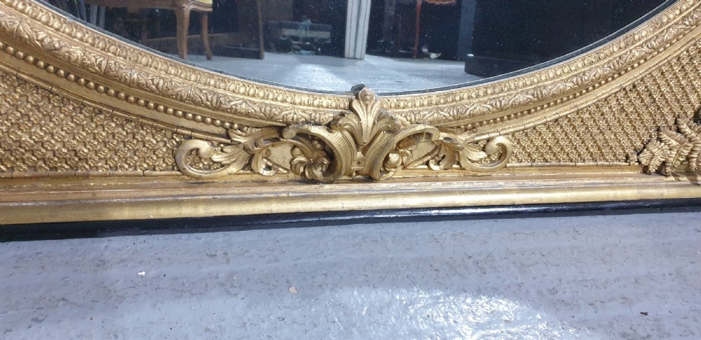 A large High Victorian arched overmantel mirror featuring a gold gilded frame decorated with carved fern leaf motifs, floral cresting, and geometric spandrel detailing. View V