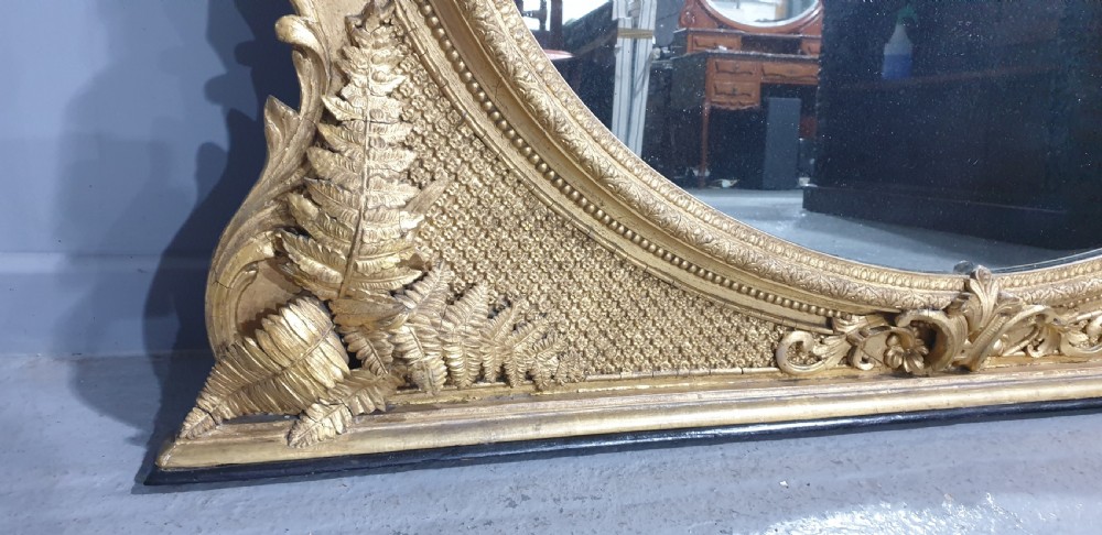 A large High Victorian arched overmantel mirror featuring a gold gilded frame decorated with carved fern leaf motifs, floral cresting, and geometric spandrel detailing. View VIII