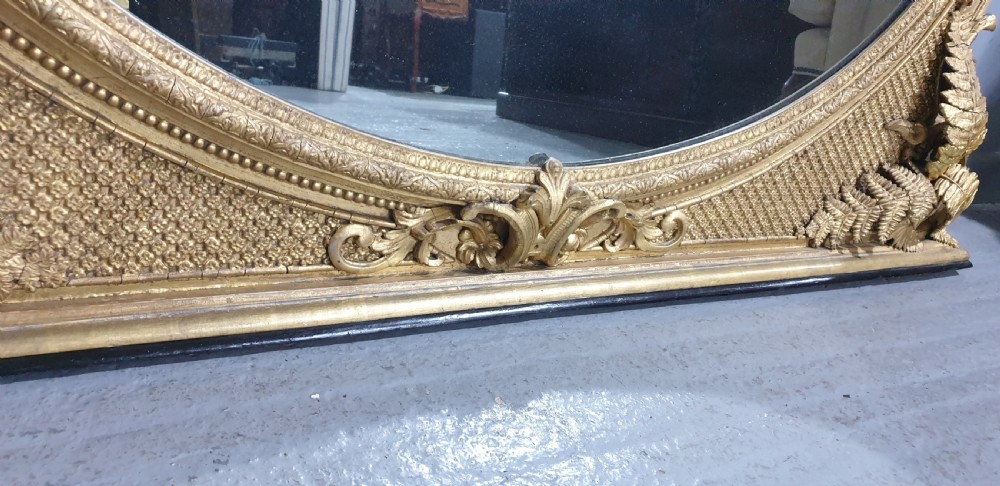 A large High Victorian arched overmantel mirror featuring a gold gilded frame decorated with carved fern leaf motifs, floral cresting, and geometric spandrel detailing. View X