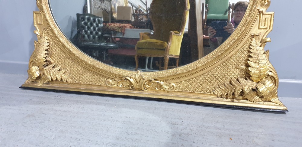 A large High Victorian arched overmantel mirror featuring a gold gilded frame decorated with carved fern leaf motifs, floral cresting, and geometric spandrel detailing. View XII