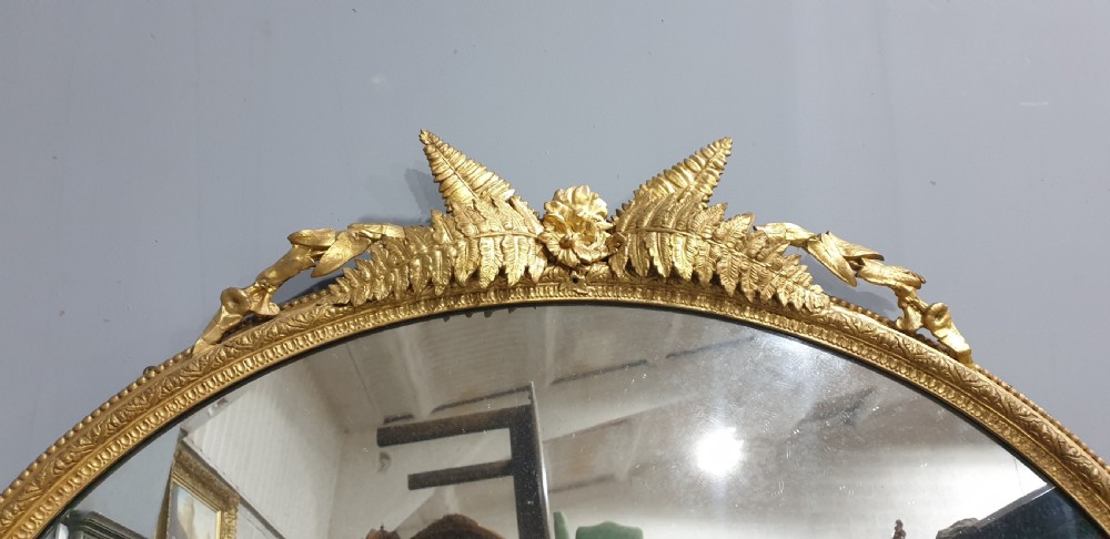 A large High Victorian arched overmantel mirror featuring a gold gilded frame decorated with carved fern leaf motifs, floral cresting, and geometric spandrel detailing. View XIV
