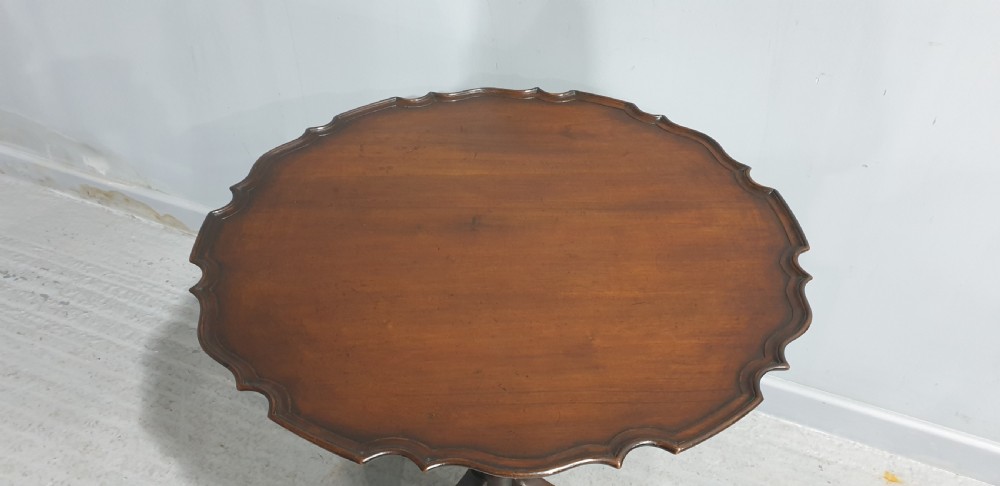 A Georgian style mahogany tilt-top table shown with the scalloped piecrust top folded vertically on a turned pedestal column with three carved legs. View III