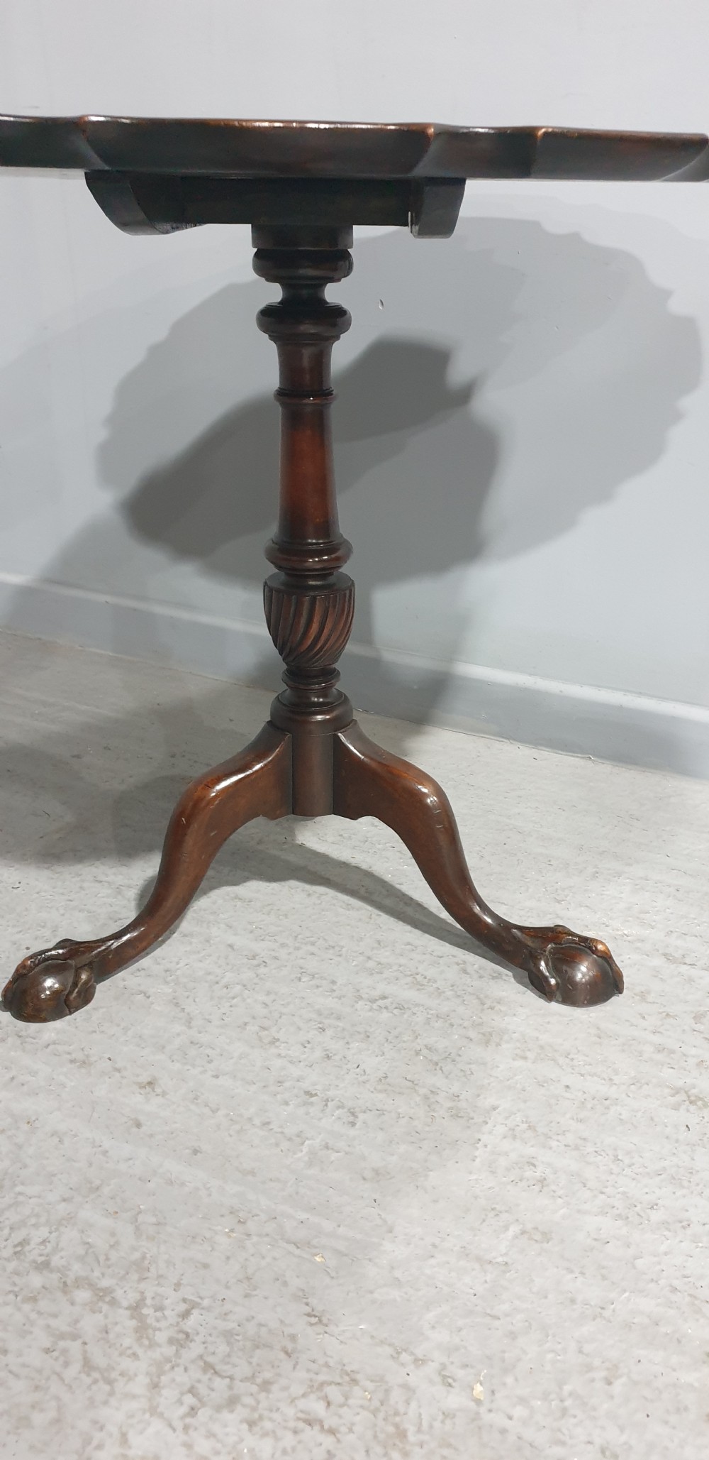 A Georgian style mahogany tilt-top table shown with the scalloped piecrust top folded vertically on a turned pedestal column with three carved legs. View IV