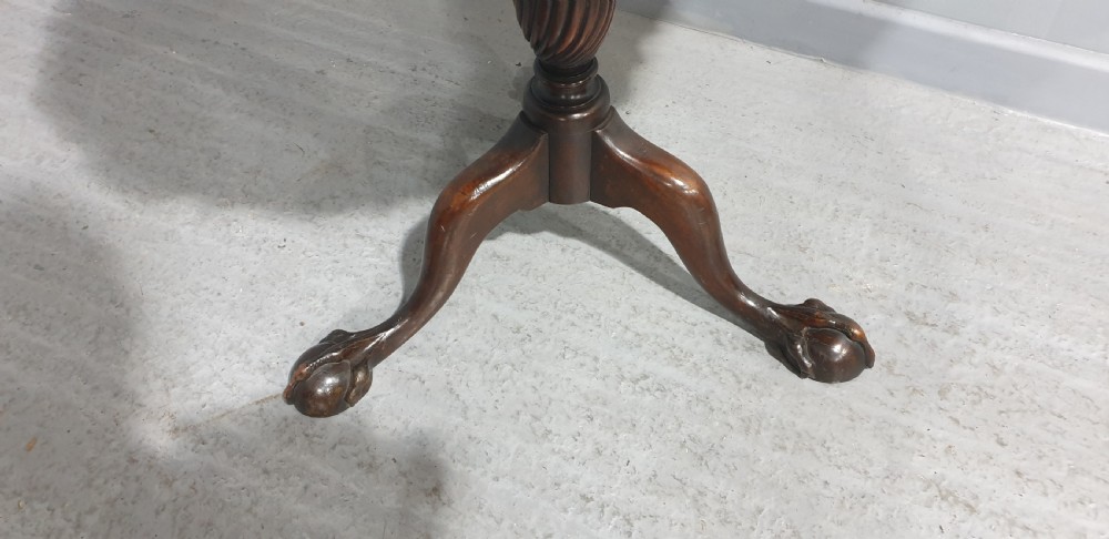 A Georgian style mahogany tilt-top table shown with the scalloped piecrust top folded vertically on a turned pedestal column with three carved legs. View V