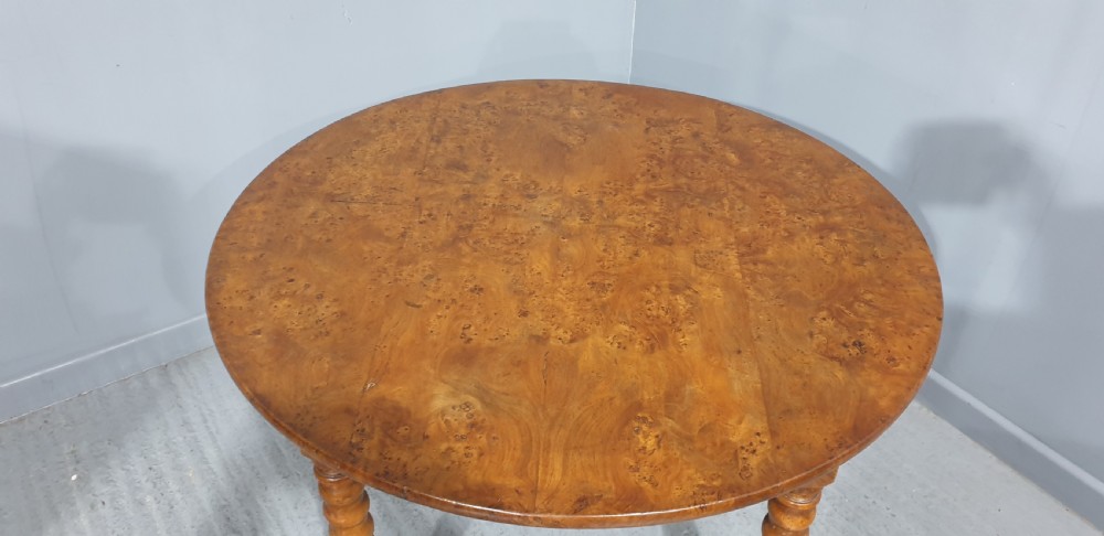 An antique round French elm dining table featuring figured wood grain, turned legs, and brass castors. View II