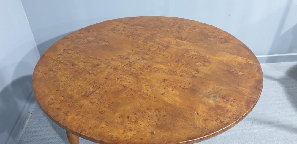 An antique round French elm dining table featuring figured wood grain, turned legs, and brass castors. View III