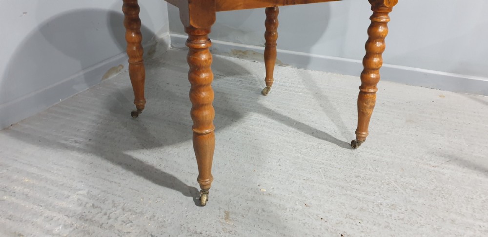 An antique round French elm dining table featuring figured wood grain, turned legs, and brass castors. View IV